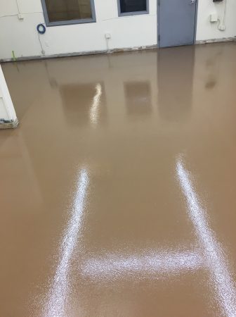 Interior view of an industrial space with a glossy tan floor showing reflections of white doors and windows, and bright white lines from overhead lighting.
