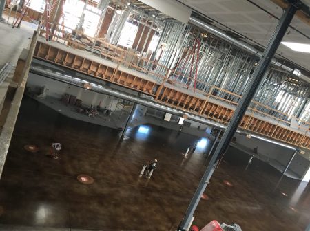 A large room with a high-shine marbled brown concrete floor, showing reflections of ceiling lights and colored walls, with a fire extinguisher mounted on a column, giving the space a functional yet polished appearance.