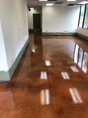 An empty room with shiny concrete floors reflecting the light from an open door at the end, showing a contrast between the illuminated and shaded areas, with electrical outlets and white walls suggesting an unfinished interior space.