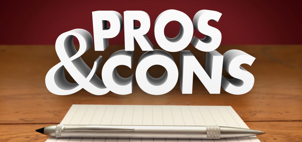The words 'PROS & CONS' in large, bold, 3D letters appear to float above a notebook and a pen on a wooden surface. The background has a warm, dark red tone that contrasts with the white text, emphasizing the theme of weighing different sides of an argument or decision.
