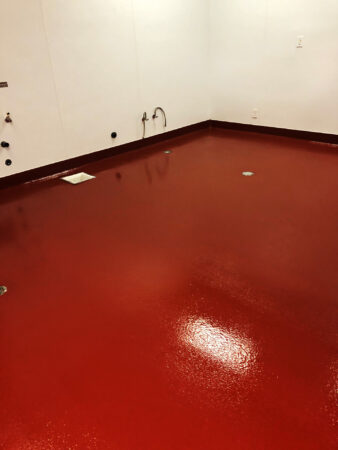 A room with glossy red epoxy flooring reflecting overhead lighting, featuring clean white walls with multiple water outlets, possibly in a commercial or industrial setting.