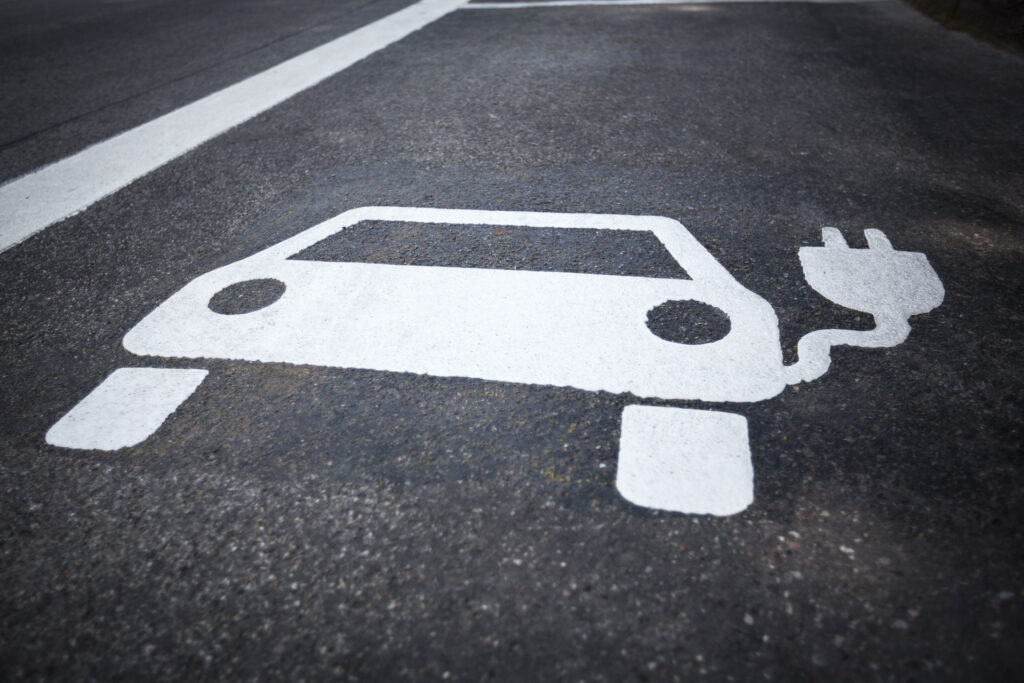 Painted symbol on concrete asphalt depicting an electric vehicle with a plug, indicating a parking space designated for charging electric cars.