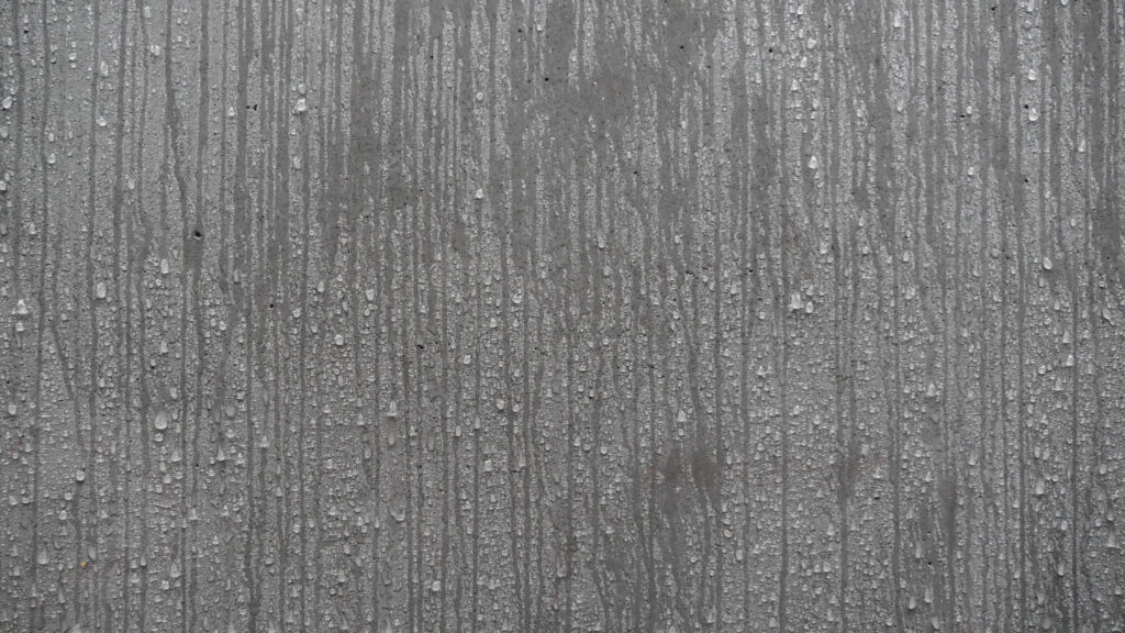 Close-up of vertical streaks and water droplets on a concrete, showing moisture on the material.
